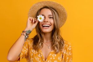 attractive stylish woman in yellow dress and straw hat holding daisy flower