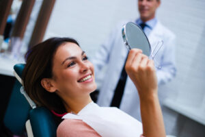 Beautiful young woman looking at mirror with smile in dentist’s office
