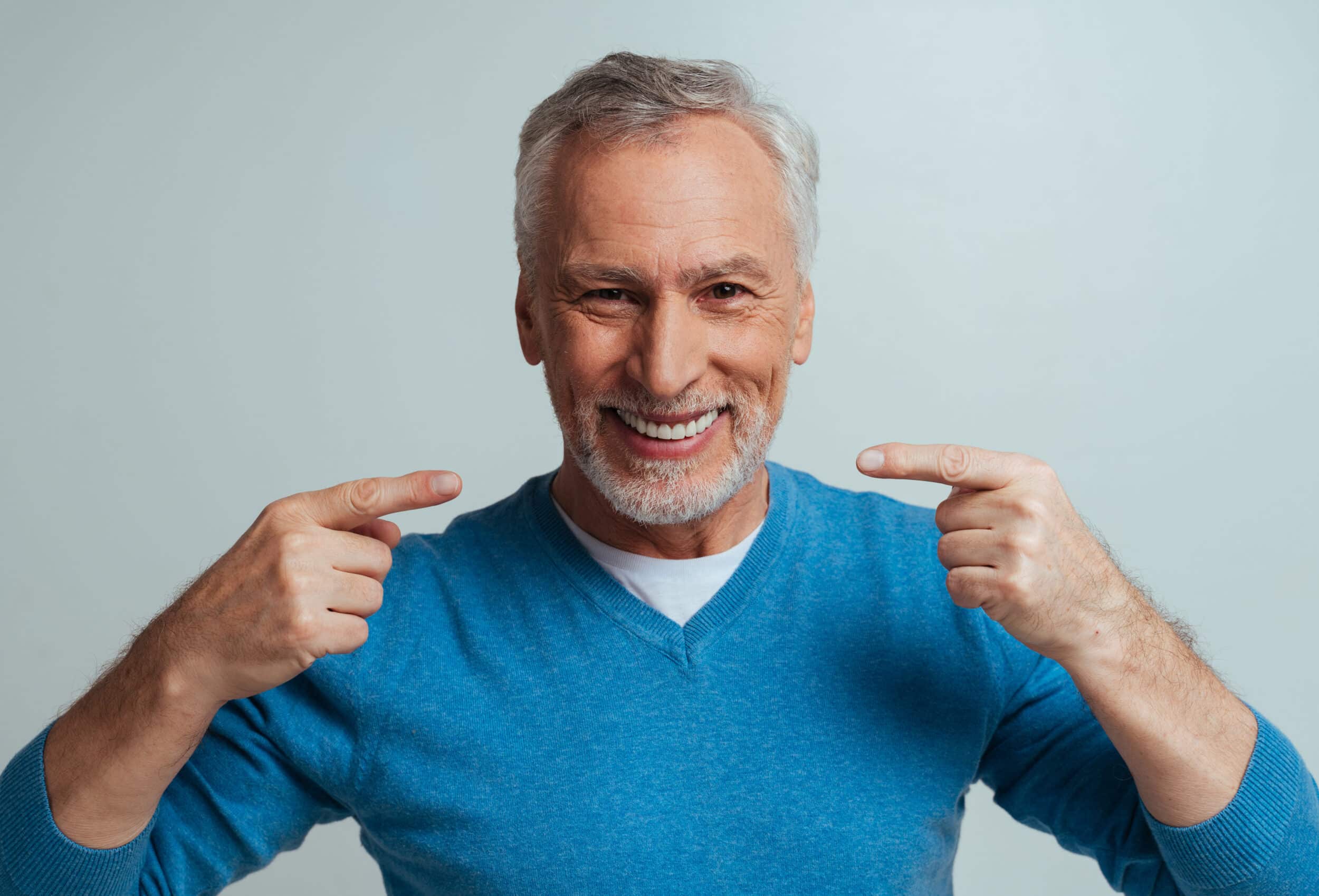 Older man smiling and pointing to his nice teeth after restorative dentistry in Milwaukee, WI